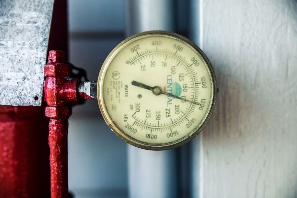A brass-rimmed water pressure gauge marked in psi and kPa mounted on a red painted supply pipe