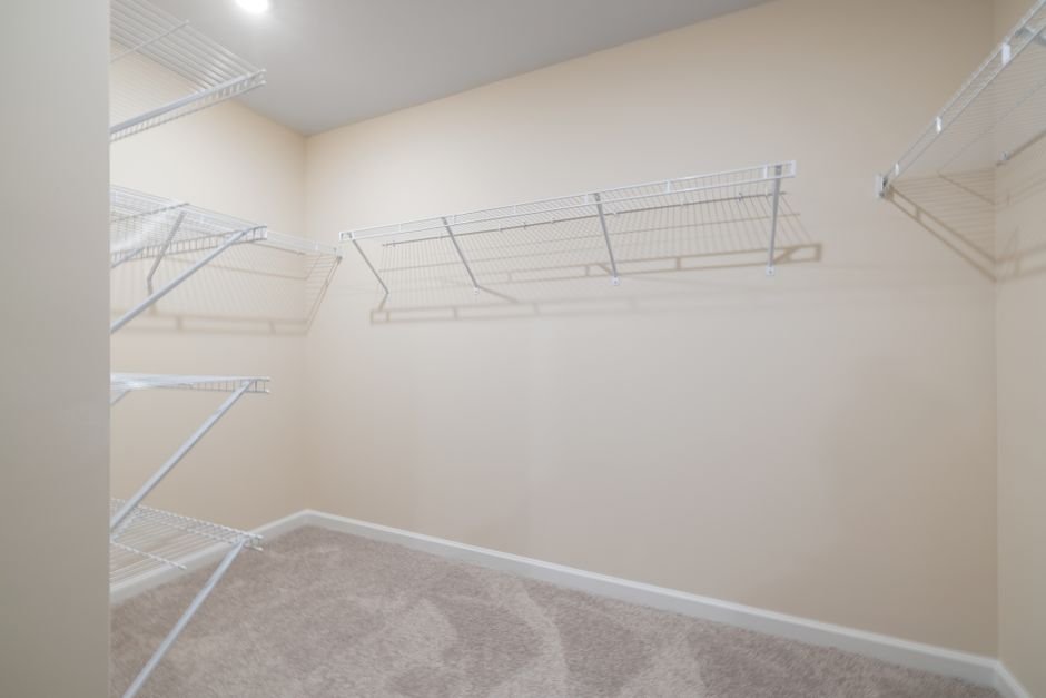 An empty reach-in closet with white wire shelving along three cream walls and carpet on the floor, the kind of space people measure for a washing machine