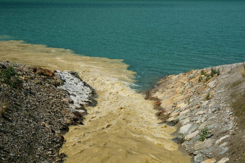 A heavily silted yellow-brown stream pouring into clear turquoise water at a rocky bank